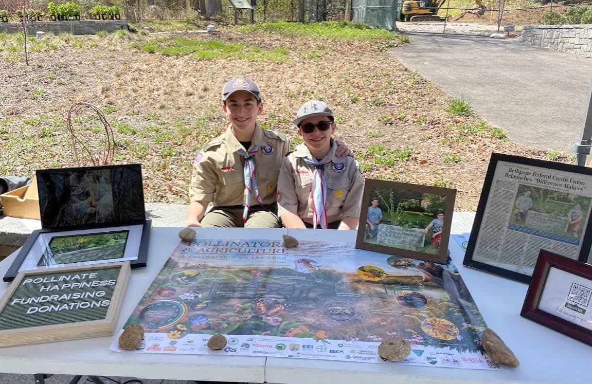 Aidan and Ben in scout uniforms at a fundraising table with photos of their project