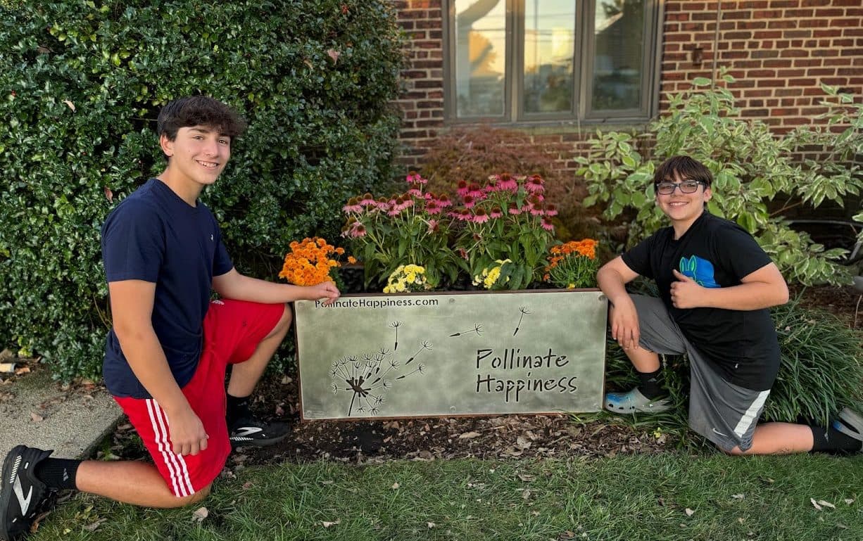 Aidan and Ben Ellis kneeling beside the Hicksville Public Library pollinator planter full of coneflowers